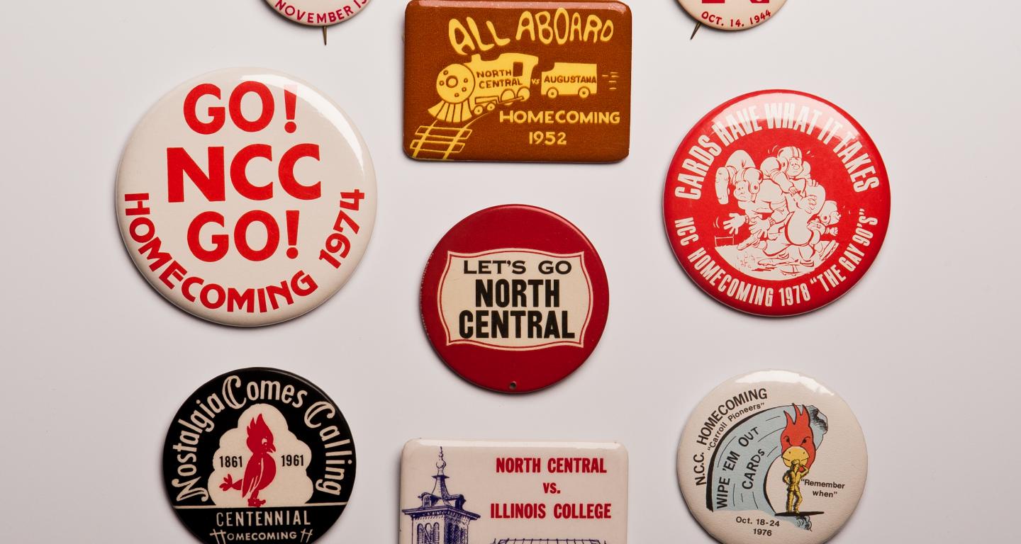 A variety of metal buttons from North Central College homecoming games scattered on a white background