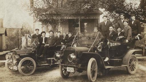 A group of young people in two 1930s automobiles